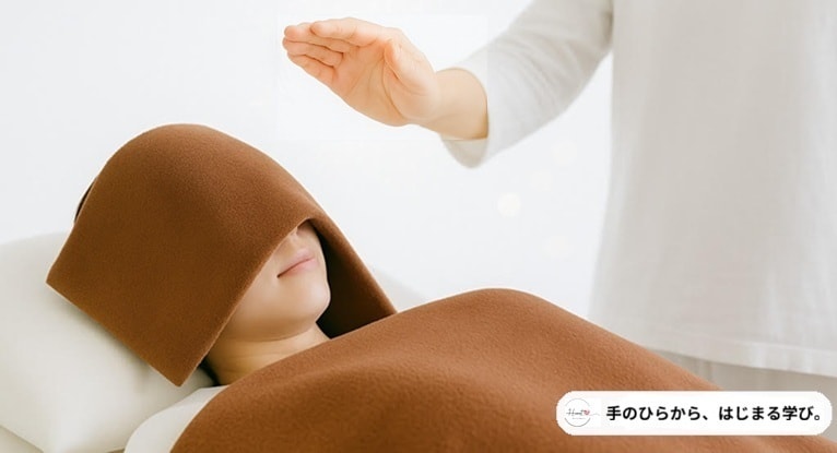 東京赤坂クイーンズティーのレイキ伝授セミナーで、タオルをかぶって横になり手のひらのエネルギーを受け取る女性