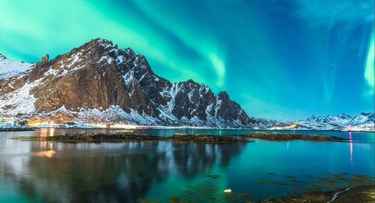 雪の山並みと静かな入り江の上に青緑のオーロラが揺らめく夜空で、レイキと自然エネルギーの調和をイメージした写真